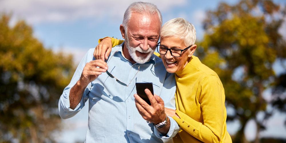 Zwei Senioren gucken auf ein Smartphone und lächeln 