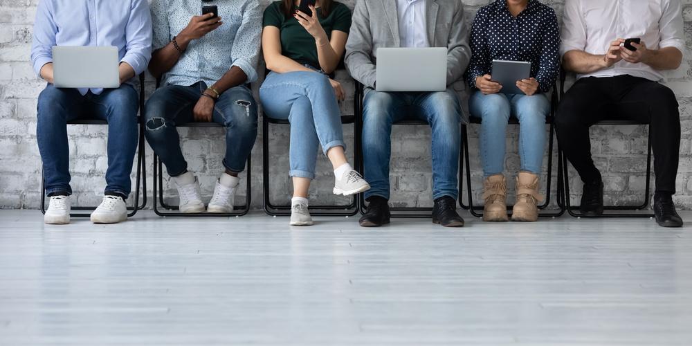 Mehrere Personen sitzen nebeneinander und nutzen Smartphones, Tablets und Laptops